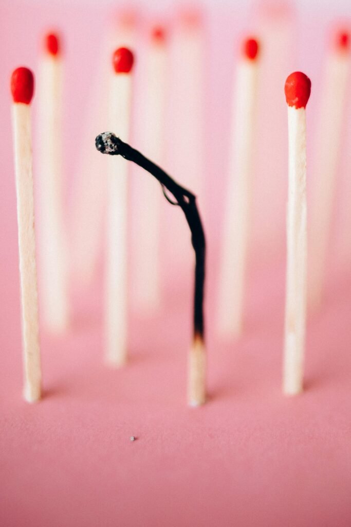 Close-up of a burnt matchstick amidst unburned ones on a pink surface, symbolizing uniqueness.